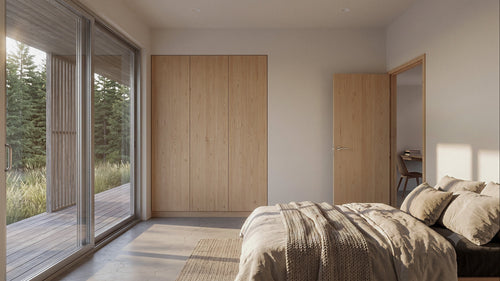 A modern bedroom interior with light wood wardrobe doors, a bed with neutral bedding, and large floor-to-ceiling windows looking out onto trees and a wooden deck.