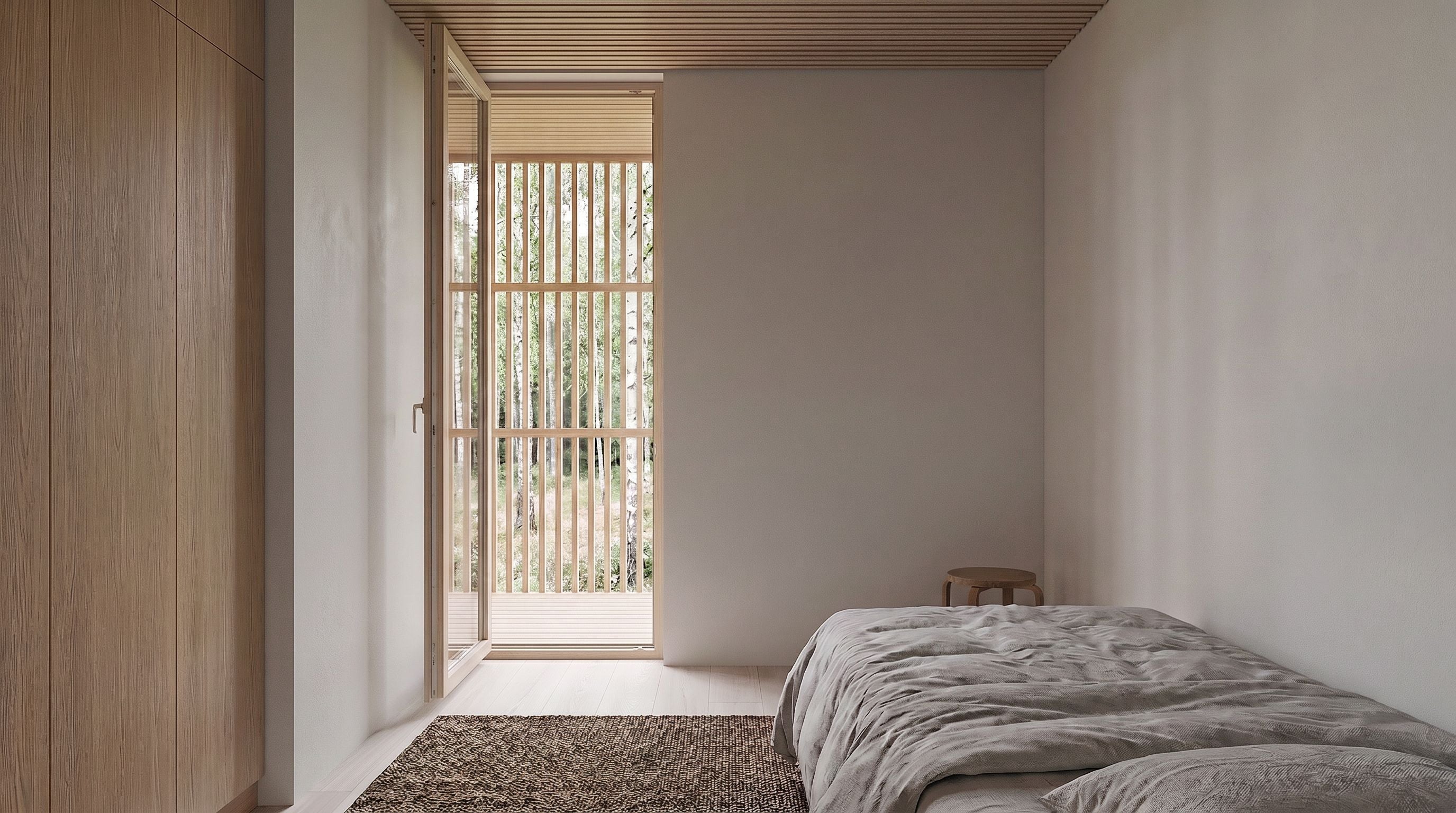 A minimalist bedroom interior with a low bed dressed in light gray bedding, a textured brown rug, a tall light wood wardrobe on the left, and an open doorway looking out onto bamboo blinds and greenery.