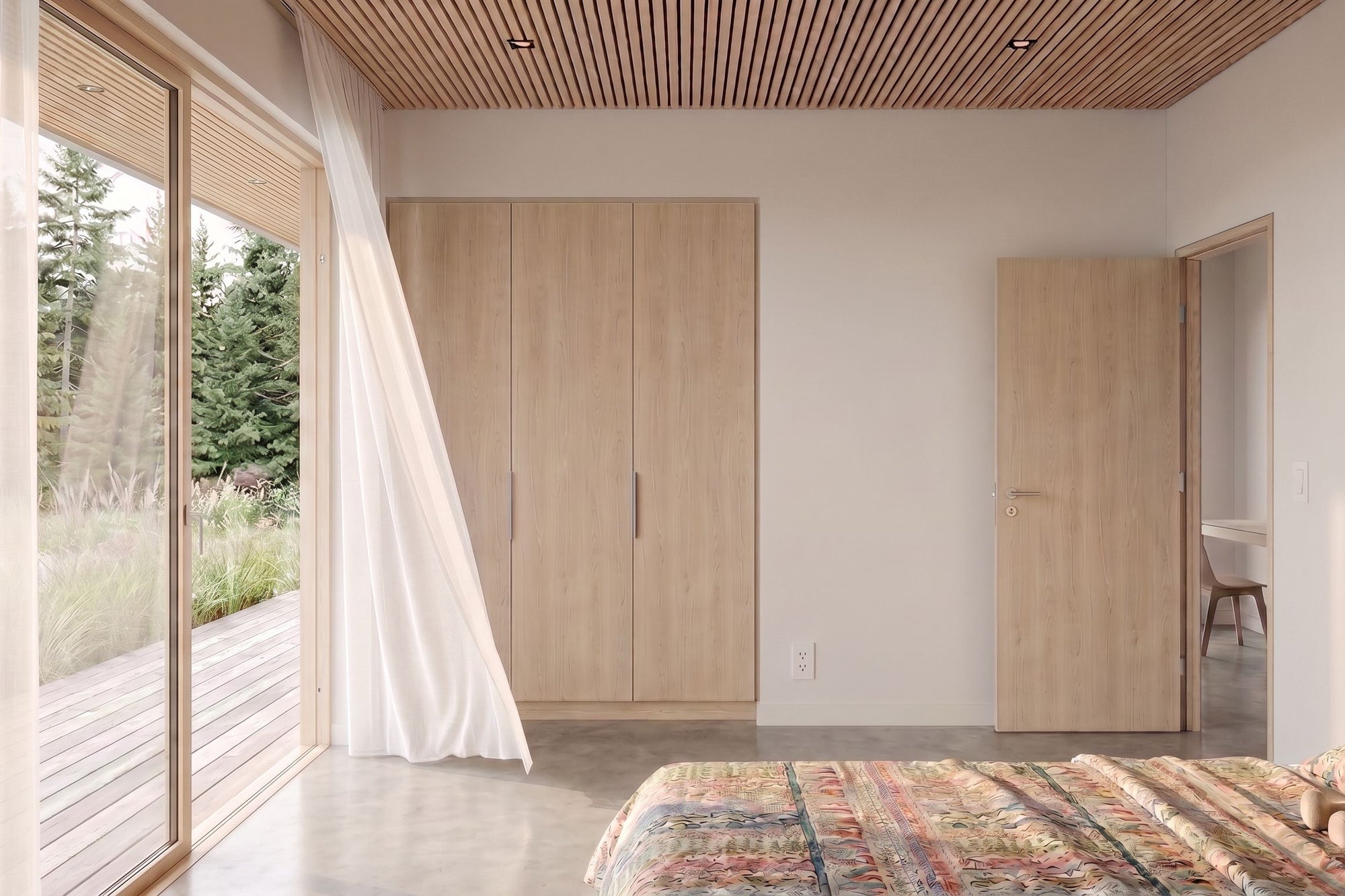 A modern bedroom interior featuring light wood furniture, including a tall wardrobe, a door, and a slatted wood ceiling, with a bed and patterned rug in the foreground and a large window looking out to trees.